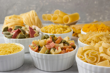 Pasta of different types in bowls on a wooden table.