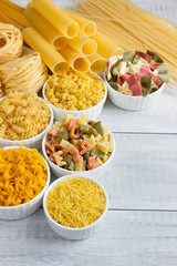 Pasta of different types in bowls on a wooden table.