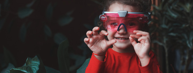 Portrait of playful smiling child girl wearing VR headset toy on background of green flowers.