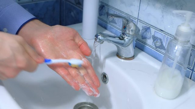 Man is washing hands with antibacterial soap and toothbrush against coronavirus in sink, hands closeup. Infection covid-19 pandemic. Hygienic procedures at home. Obsessive compulsive disorder symptom.
