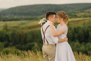 Loving bride and groom embrace bowing their heads to each other, against the backdrop of a beautiful landscape.
