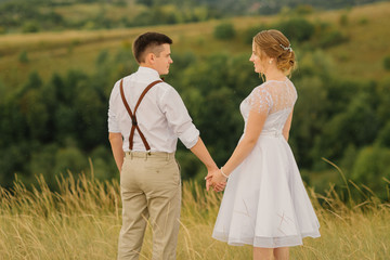 Happy bride and groom holding hands and standing in front of a beautiful view of nature. Wedding day.