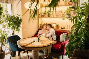 Happy bride and groom cuddling. Sitting on a sofa in a cozy cafe on their wedding day.