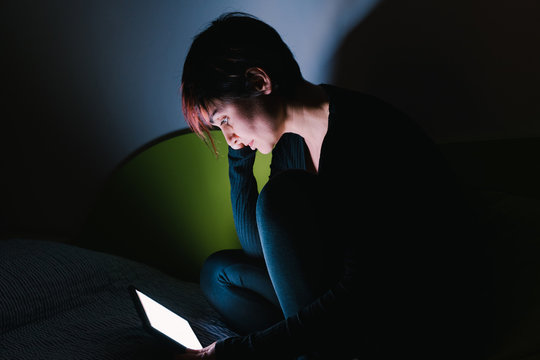 Young Woman Watching Online Tv Show In Bed At Night. People Hooked Up With Entertainment Devices Before Going To Bed. Technology And Leisure Concept. Lifestyle At Home For Young People.