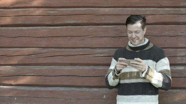 Happy young man using phone against wooden wall in autumn
