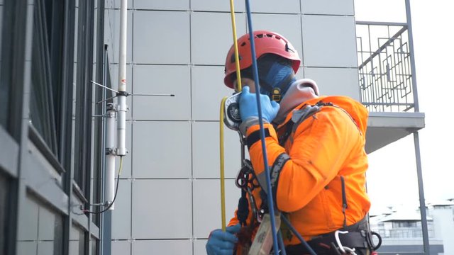 industrial climber in rubber gloves slides down rope using descent device outside tall building, high-rise work