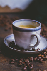Granos de cafe por la mesa de madera rústica. Un expresso en una taza blanca. De fundo se ve un moledor. La imagen es acogedora, caliente, vintage.