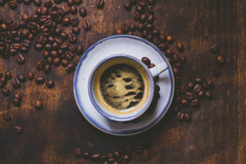 Granos de cafe por la mesa de madera rústica. Un expresso en una taza blanca. De fundo se ve un moledor. La imagen es acogedora, caliente, vintage.