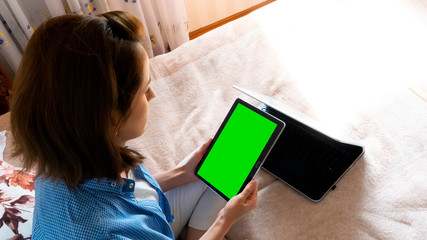 Fototapeta na wymiar a happy girl sits on a bed and holds a tablet in her hands, she communicates via video communication in quarantine and sits at home. isolated background on tablet