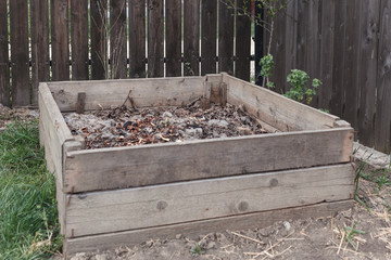 Compost box. Humus. Organic waste. Wooden compost box with leaves inside on wooden fence background