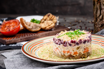 Herring under a fur coat, a salad of salted herring fillet, boiled potatoes, beets, carrots, fresh onions and mayonnaise on a white plate on a wooden background