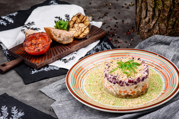 Herring under a fur coat, a salad of salted herring fillet, boiled potatoes, beets, carrots, fresh onions and mayonnaise on a white plate on a wooden background