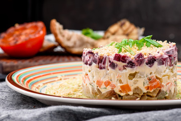 Herring under a fur coat, a salad of salted herring fillet, boiled potatoes, beets, carrots, fresh onions and mayonnaise on a white plate on a wooden background
