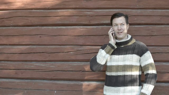 Happy young man talking on the phone against wooden wall in autumn