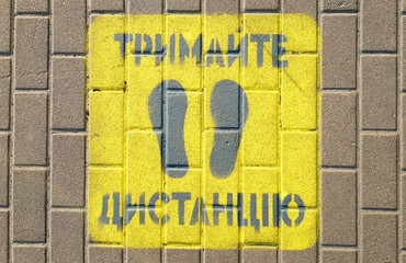 Fototapeta premium Yellow sidewalk with the warning Keep your distance on the sidewalk. The text is in Ukrainian. Concept of maintaining social distance, quarantine or isolation.