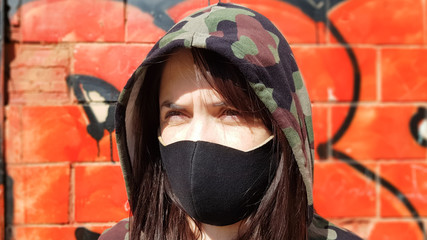 Portrait of a woman in a protective black mask outdoors near an old broken wall. Coronavirus and air pollution concept. A girl wears a protective mask to protect against a pandemic.