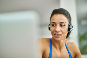 Naklejka premium Young sportswoman with headset using computer at home.