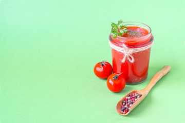Tomato juice with a leaf of parsley in a glass jar, fresh tomatoes and a wooden spoon with pepper. Light green background, copy space.