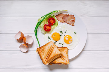 Plate with fried eggs, bacon, tomatoes with bread, onion on a ru
