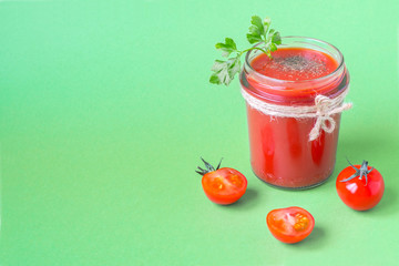 Tomato juice with a leaf of parsley in a glass jar and fresh tomatoes. Light green background. copy space.