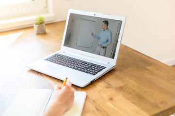 A man conducts online classes, webinars on the laptop screen, hands of woman doing notes in notebook