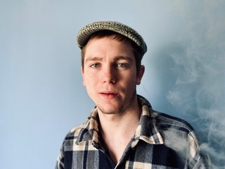 a young  man in checked shirt and retro hat smoking electronic cigarette