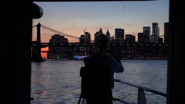 Travel blogger spending time for exploring American megalopolis with boat sightseeing using smartphone gadget for photographing evening cityscape, concept of journey vacations in USA

