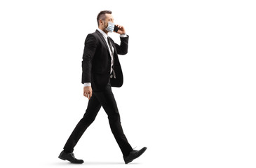 Obraz premium Businessman talking on a mobile phone, walking and wearing a protective medical mask