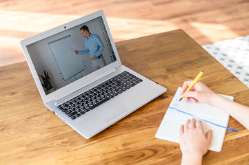 Female hands writing a syllabus in notebook, a laptop with a online lecture on the table. Concept...