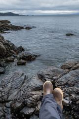 Feet with boots looking at pacific ocean water beach