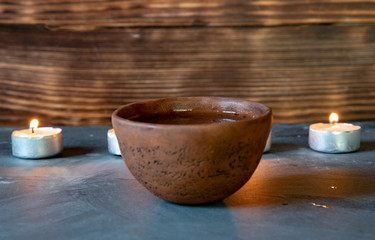 A ceramic bowl with tea and burning candles on a gray tabletop.