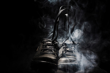 pair of used sports shoes with the laces untied fuming. sports concept. black background