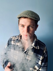 a young  man in checked shirt and retro hat smoking electronic cigarette