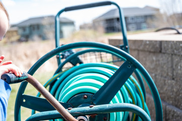 Selective focus on front bar on a wound garden hose storage cart with small child spinning lever