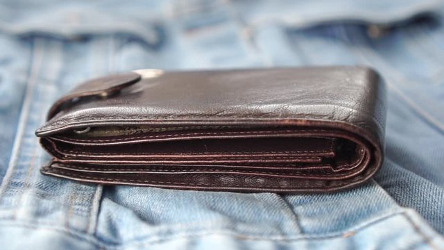 Empty brown wallet falls on jeans clothes. Leather accessory. The concept of the financial crisis due to the coronavirus pandemic
