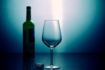 Empty wine glass, on a background a wine bottle. In the light of the blue lamp