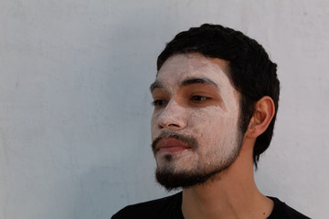 portrait of young Hispanic man with a beard wearing a hydrating mask on a white background