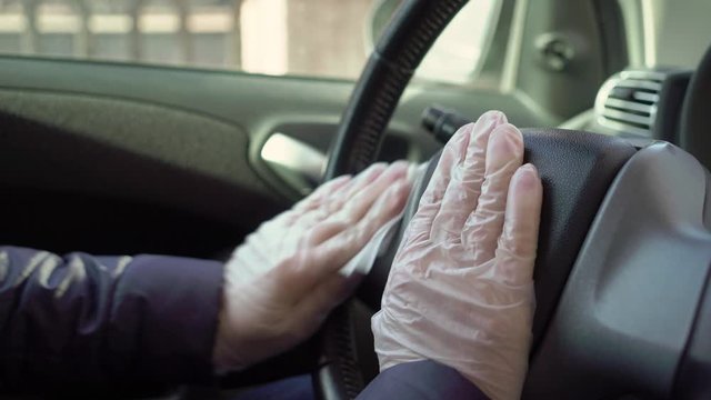 Young woman clean steering whell of car in protective gloves.