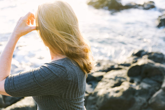 Middle Aged Boomer Woman Standing At Ocean Shore Looking Out At Sunset View