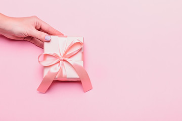 Woman holding pink gift box on pastel background, copyspace. Mother's Day or Women's Day card in trendy colors, top view