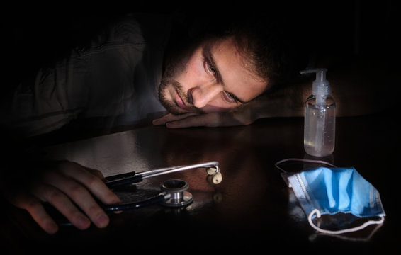Coronavirus: Young bored and sad doctor with protective mask looking at the stethoscope