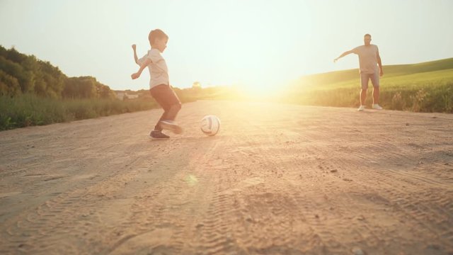 Young father with his little son are having fun and playing football on green grassy lawn at sunset