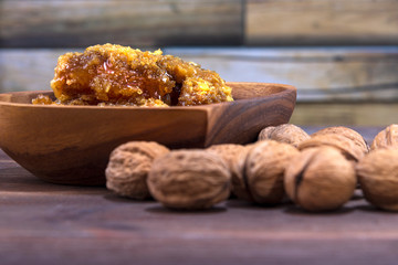 Honeycombs with honey in a wooden plate and many inshell walnuts on a wooden surface