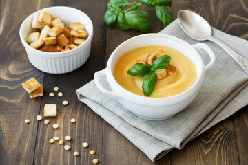 Cream soup of peas with greens and croutons on a brown wooden background.