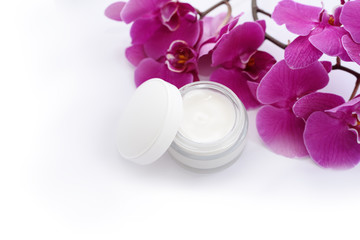 Opened jar of facial cream with many orchidee flowers.