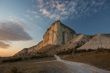 White rock against a beautiful sunset, light clouds fly over the rock and the road leads to the foot of the rock.