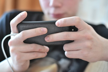 The young man enthusiastically plays on the phone, holding it in his hands, sitting at home during...