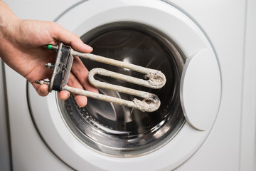 Person holds in his hand a damaged electric heating element from the washing machine. Repair and restoration work