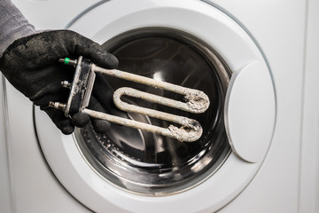 Person holds in his hand a damaged electric heating element from the washing machine. Repair and restoration work