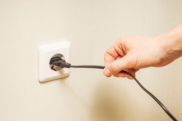 A person’s hand pulls an electrical cord plugged into a power outlet
